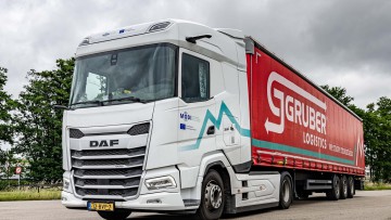 Ein DAF Lkw mit Gruber Logistics-Anhänger unter bewölktem Himmel steht auf der Straße.