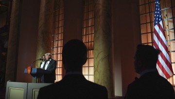 Donald Trump spricht beim Dinner im Building Museum, am Sonntag den 19. Januar 2025, in Washington, Ehefrau Melania Trump im Hintergrund und weitere Leute hören zu, rechts die amerikanische Flagge