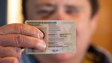 Mann hält Ausweis mit ausgestrecktem Arm in die Kamera und verdeckt so sein Gesicht