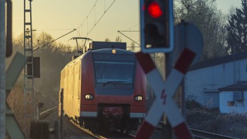 Eine rote Ampel sperrt einen Bahnübergang wegen eines herannahenden Zuges.