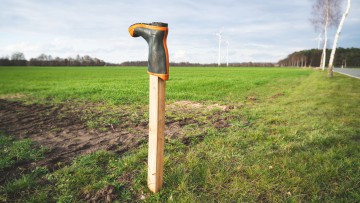 Gummistiefel über Pfahl gestülpt auf Feld vor Windrädern am Horizont