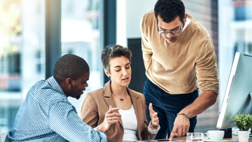 Zwei Männer und eine Frau diskutieren in einem Büro über einem Tablet