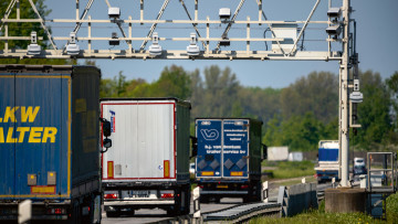 Lkw fahren auf der Autobahn unter einer Maut-Kontrollbrücke hindurch.