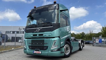 Seitliche Frontansicht des neuen Volvo FM Electric. Das türkis lackierte 6x2-Fahrgestell ist mit einem Abrollaufbau der Firma Meiller ausgestattet