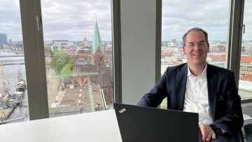 Tobias Jerschke von Kühne + Nagel sitzt an seinem Laptop am Schreibtisch und lächelt in die Kamera.