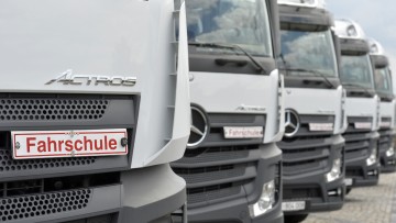 weiß lackierte Lkw der Marke Mercedes Actros stehen in einer Reihe, auf jedem steht an der Front unterhalb des Fensters das Schild "Fahrschule"