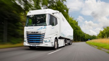 Ein in weiß lackierter XF Electric fährt über eine sommerliche Landstraße. Die Sattelzugmaschine hat einen ebenfalls weißen Kofferaufliger aufgesattelt 