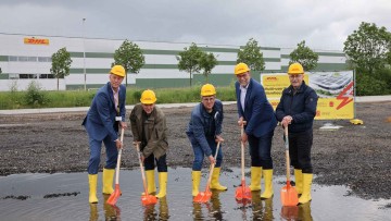 Verregneter Spatenstich: Dirk van Houtum (DHL), Hans van de Winkel (Gemeinde Sittard-Geleen), Huub Menten (Gemeinde Sittard-Geleen), John Scherders (DHL) and Jan van de Berg (Gemeinde Sittard-Geleen) stehen mit Gummistiefeln und Schaufeln in einer Pfütze 