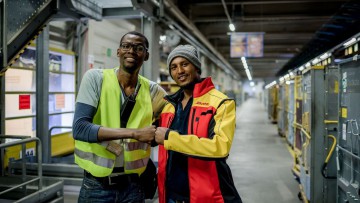 Zwei Geflüchtete DHL-Arbeiter lächeln in Arbeitskleidung in die Kamera