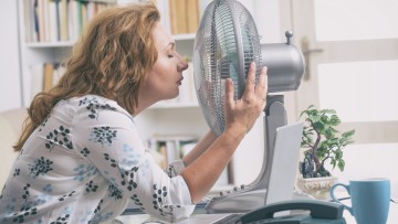Frau im Büro kühlt sich am Ventilator
