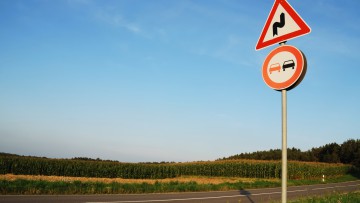 Überholverbot und Warnung vor Kurven vor idyllischer Landschaft an Landstraße