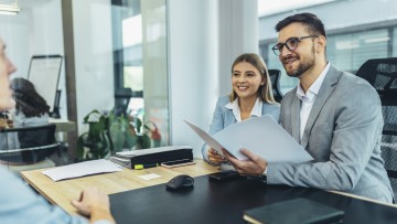 Ein Mann und eine Frau, sprechen während eines Vorstellungsgesprächs im Büro mit einem Kandidaten, der nur unscharf links zu erkennen ist. 