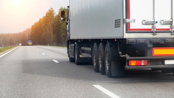 Ein Lkw mit einem weißen isothermen Sattelauflieger transportiert im Frühling Fracht vor der Kulisse eines Waldes. 