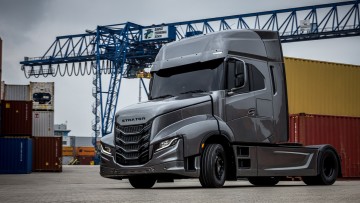 Seitliche Ansicht von links vorne des neuen Iveco Strator. Die in Silber lackierte Zweiachs-Zugmaschine parkt in einem Containerpark