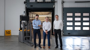 Vertreter von Jungheinrich und Navflex stehen neben einem autonomen Flurförderzeug vor der Laderampe