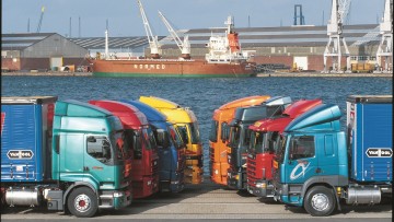 Acht Sattelzugmaschinen parken im Jahr 2000 in Reih und Glied in einem Hafengebiet