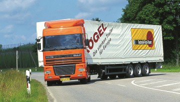 Ein in Orange lackierter DAF XF 95 beim Abbiegevorgang auf einer Landstraße. Das Fahrzeug hat einen Sattelauflieger aufgesattelt