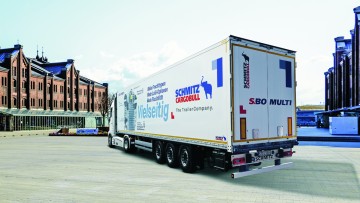 Seitliche Ansicht von hinten des neuen S.BO Multi von Schmitz Cargobull. Der dreiachsige Kofferauflieger steht in einer urbanen Umgebung, eine Sattelzugmaschine ist angehängt