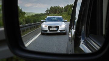 Gestellte Aufnahme: Ein Auto gibt auf der Autobahn Lichthupe und fährt nah auf. Fotografiert im Außenspiegel eines Autos.