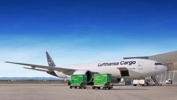 Ein Flugzeug von Lufthansa Cargo wird auf dem Flugfeld beladen. Vor dem Fkugzeug stehen zwei grüne Frachtbehälter