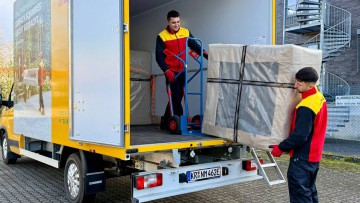 Zwei Mitarbeiter von DHL 2-Mann-Handling laden ein verpacktes Möbelstück aus ihrem Transporter