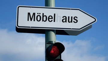 Über einer roten Ampel befindet sich ein Wegweiser mit dem defekten Schriftzug Möbelhaus.