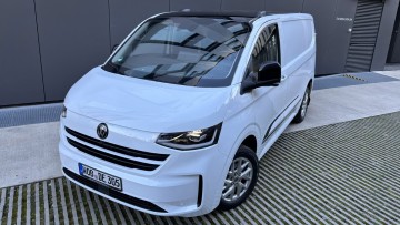 Seitliche Frontansicht des neuen Transporters. Der in weiß lackierte Kastenwagen steht vor einer modernen Lagerhalle