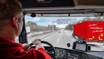 Lkw-Fahrer am Steuer sieht auf der Autobahn Lkw mit KRAVAG-Logo vor sich