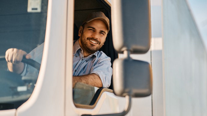 Glücklicher professioneller LKW-Fahrer, der seinen LKW fährt und in die Kamera schaut