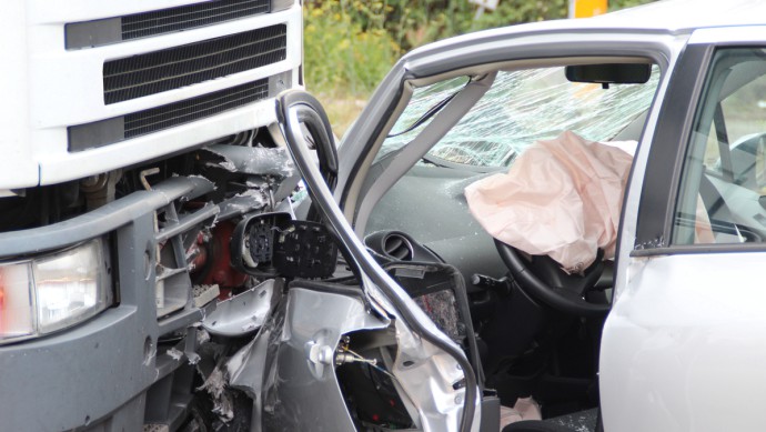 Detailaufnahme: beschädigte Front eines Lkw und ein leicht quer dazu stehender zerstörter Pkw, der sich zum Tei in die Front bohrt (Symbolbild für Unfall mit Lkw)
