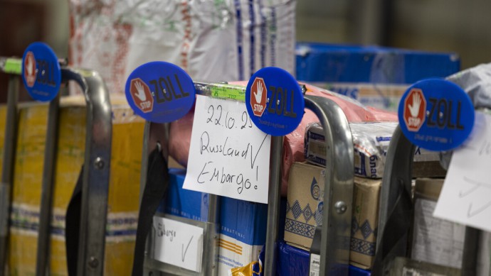 Schilder mit der Aufschrift „Zoll“ hängen an Paketwagen. "Russland Embargo" steht auf einem Paketwagen. Im Internationalen Postzentrum am Frankfurter Flughafen 2025.