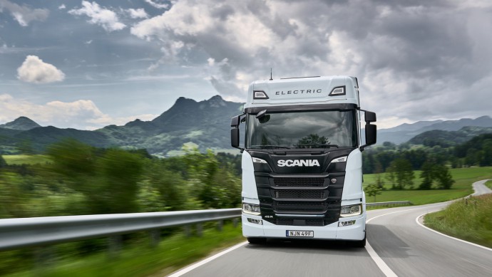 Elektro-Lkw von Scania auf der Landstraße, im Hintergrund grüne Wiesen und Berge