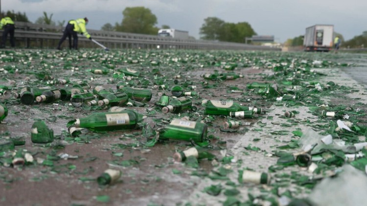 Zerstörte Bierflaschen liegen auf der Autobahn, Menschen in Warnjacken fegen, ein Lkw steht im Hintergrund