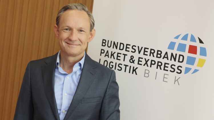 Marten Bosselmann, Vorstandsvorsitzender vom Bundesverband Paket & Expresslogistik BPEX, lächelt in die Kamera vor dem BPEX Logo