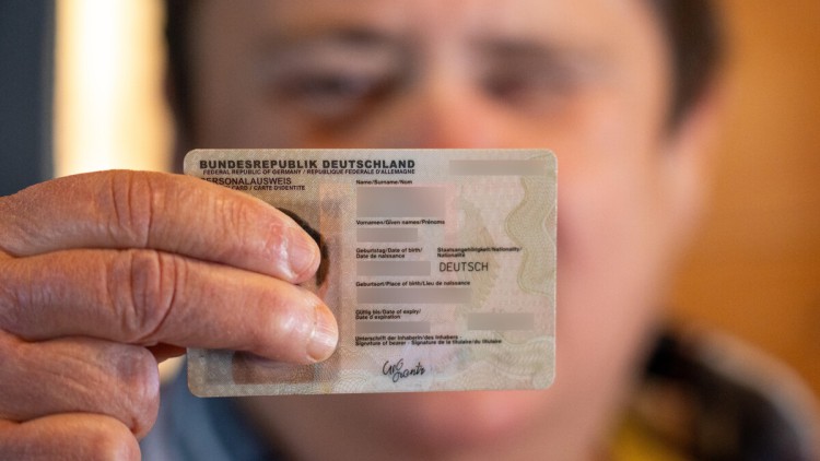 Mann hält Ausweis mit ausgestrecktem Arm in die Kamera und verdeckt so sein Gesicht
