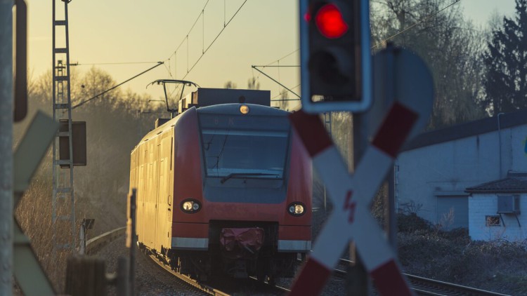 Eine rote Ampel sperrt einen Bahnübergang wegen eines herannahenden Zuges.