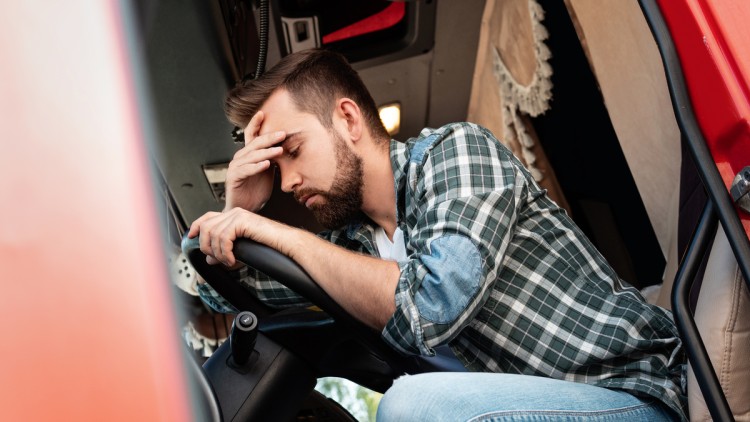 Junger Lkw-Fahrer müde oder krank über sein Lenkrad gebeugt, hält sich den Kopf