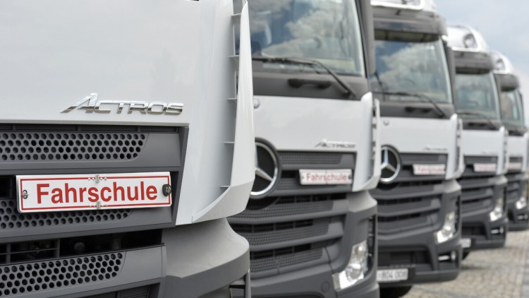 weiß lackierte Lkw der Marke Mercedes Actros stehen in einer Reihe, auf jedem steht an der Front unterhalb des Fensters das Schild "Fahrschule"