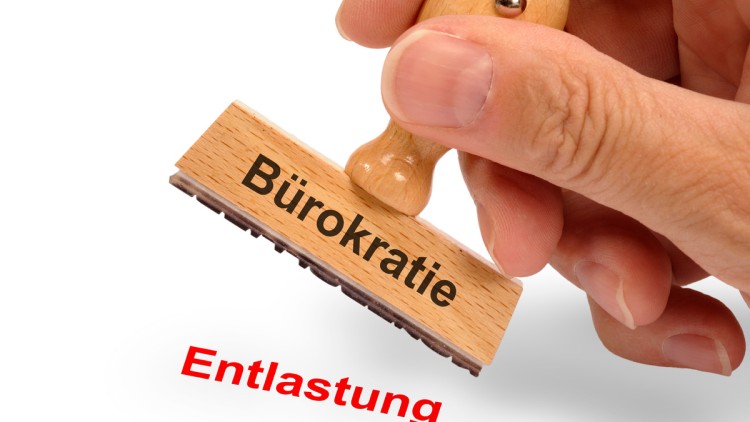 Holzstempel beschriftet mit dem Aufdruck Bürokratie und dem Abdruck Entlastung