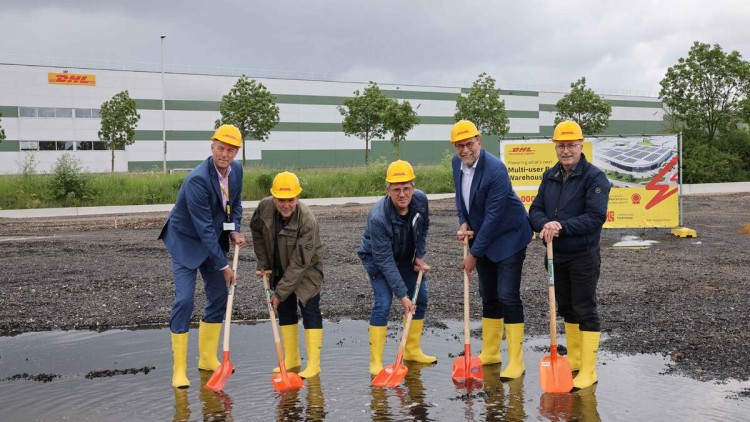 Verregneter Spatenstich: Dirk van Houtum (DHL), Hans van de Winkel (Gemeinde Sittard-Geleen), Huub Menten (Gemeinde Sittard-Geleen), John Scherders (DHL) and Jan van de Berg (Gemeinde Sittard-Geleen) stehen mit Gummistiefeln und Schaufeln in einer Pfütze 