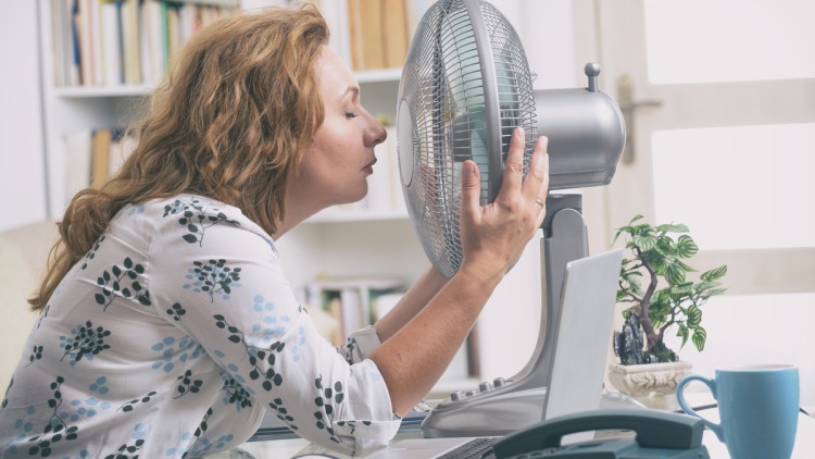 Frau im Büro kühlt sich am Ventilator