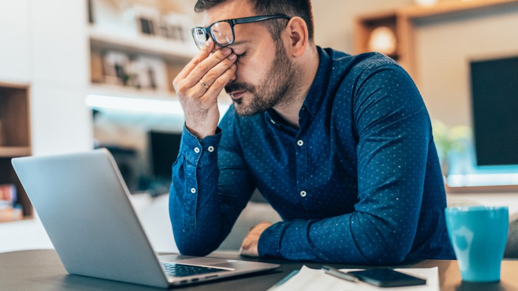 Müder junger Geschäftsmann, der zu Hause mit Laptop arbeitet und ängstlich aussieht