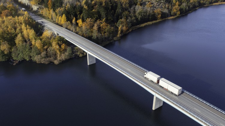 Lkw fährt auf Brücke über einen Fluss in Richtung eines herbstlichen Waldes