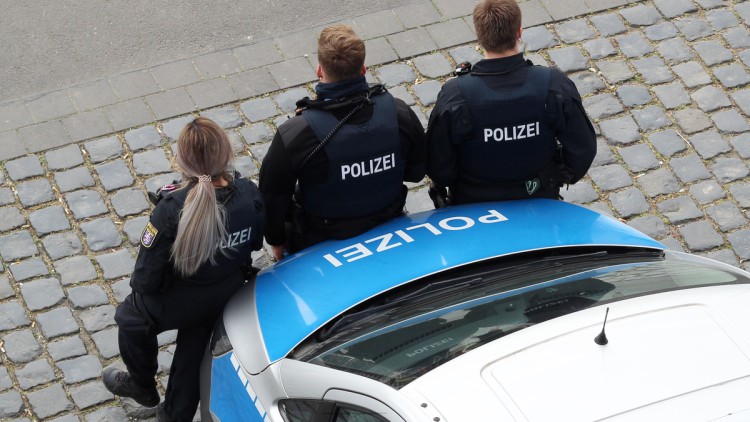 Drei Polizisten lehnen an ein Polizeiauto