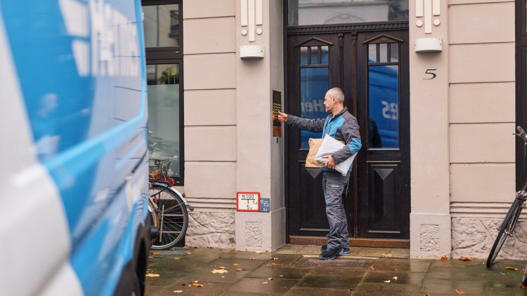 Ein Paketzusteller von Hermes klingelt mit einem Paket unter dem Arm an einer Haustür