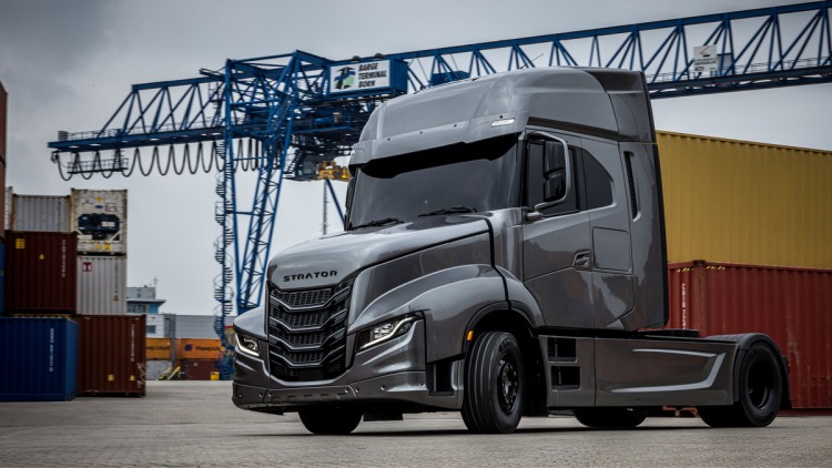 Seitliche Ansicht von links vorne des neuen Iveco Strator. Die in Silber lackierte Zweiachs-Zugmaschine parkt in einem Containerpark