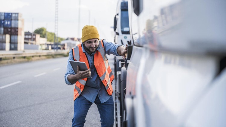 Ein junger Mann mit Warnweste und eine Tablet-PC untersucht einen geparkten Lkw. Symbolbild für Begutachtung eines Schadens