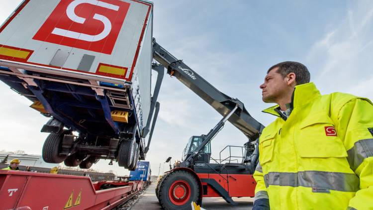 Ein Mann sieht dabei zu, wie ein Kran einen Container auf ein Podest hebt