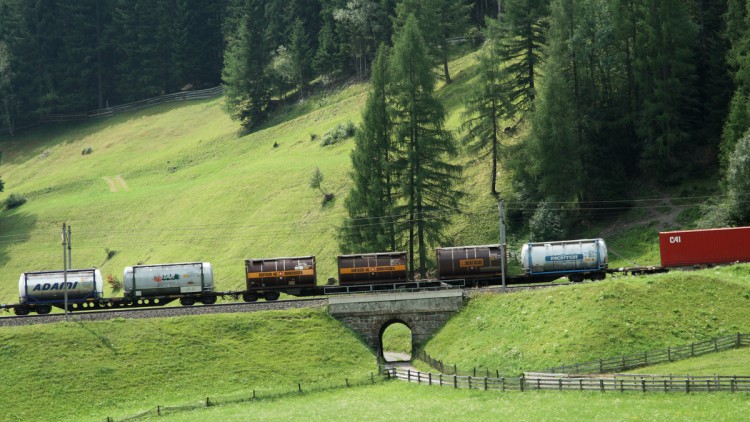 Eine Güterzug fährt bei Sonnenschein an einer grünen Landschaft vorbei