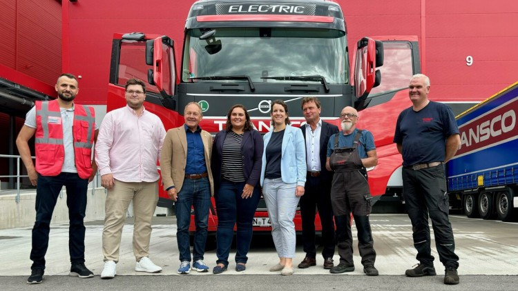 Acht Menschen stehen vor einem roten Elektro-Lkw und lächeln in die Kamera